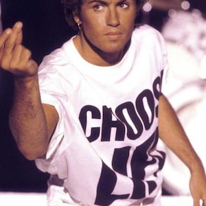 Op de afbeelding: Een persoon draagt een wit t-shirt met de woorden "CHOOSE LIFE" in grote zwarte letters. De persoon draagt ook een witte broek. De afbeelding is een medium shot, met de persoon in het midden.