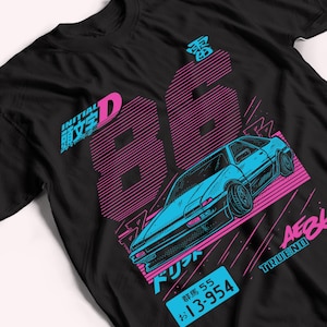 Pode incluir: Uma t-shirt preta com uma impressão gráfica de um carro desportivo azul. O design inclui o número 86 grande em rosa, o texto Initial D, AE86 Trueno e uma matrícula azul com o texto 13-954 e caracteres japoneses.