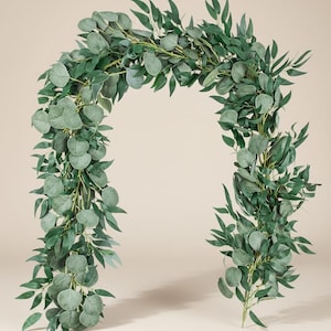 May include: A vibrant green eucalyptus garland, shaped into an arch. The garland is composed of a variety of leaf shapes, including rounded and elongated leaves, providing a dense and textured look. Suitable for weddings, home decoration, or event design.