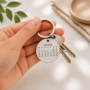 Puede incluir: Un llavero circular de metal plateado con un calendario grabado de junio de 2024. El texto dice JUN 2024 con los días de la semana y las fechas del 1 al 30. Un pequeño corazón rodea el número 8. Dos llaves de metal están adjuntas.