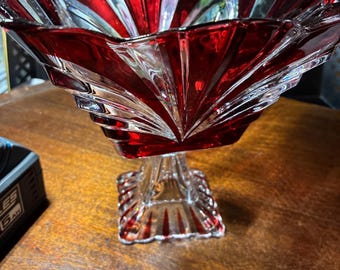Peut inclure: Un bol à pied vintage en verre rouge et transparent. Le bol présente un motif en étoile avec des accents rouges et une base carrée. Le bol est probablement utilisé pour servir ou exposer.