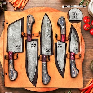 May include: A set of six kitchen knives with wooden handles and patterned blades, displayed in a leather sheath. Each knife has a personalized initial. The handles are a mix of dark and light wood, with red accents.