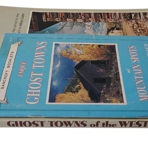 Op de afbeelding: Een stapel vintage boeken getiteld "Ghost Towns of the West" en "Unique Ghost Towns". Het bovenste boek is lichtblauw met een afbeelding van een hut en de tekst "Unique Ghost Towns and Mountain Spots".