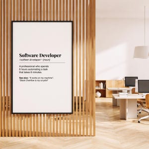 Pu&ograve; includere: Una stampa incorniciata con la definizione di "Software Developer" in testo nero. La definizione include la pronuncia fonetica, una descrizione del lavoro e frasi correlate. La stampa &egrave; esposta su una parete a doghe di legno.