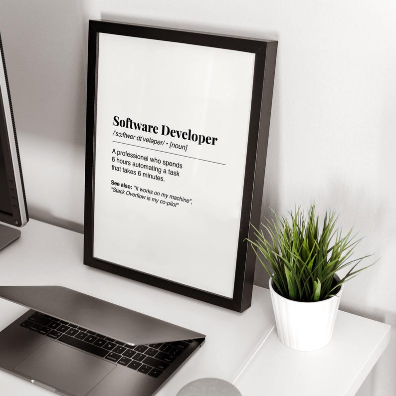 Pu&ograve; includere: Una stampa incorniciata con la definizione di "Software Developer" in testo nero su sfondo bianco. La cornice &egrave; nera e la stampa &egrave; esposta su una scrivania bianca accanto a un laptop e una piccola pianta in vaso.