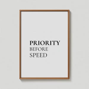 May include: A framed print featuring the text "PRIORITY BEFORE SPEED" in black on a white background. The frame is a warm brown colour. This minimalist artwork is suitable for home or office decoration, with a simple, elegant design.