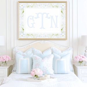May include: A rectangular wall art print in a gold frame featuring the letters G, T, and N in a light blue striped font. The print has a white center and a border decorated with a light blue and green floral pattern on a white background.
