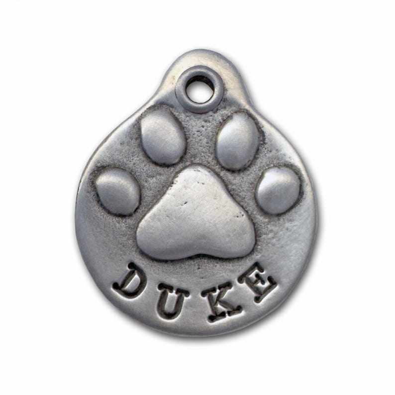 May include: Silver dog tag featuring a paw print design with the name "DUKE" engraved on it.