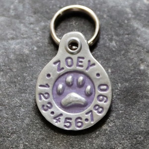 May include: Silver dog tag with a purple paw print and the name "ZOEY" engraved on it. The tag has numbers 1, 2, 3, 4, 5, 6, 7, 8, 9, and 0 around the edge.