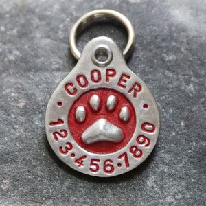 May include: Silver dog tag with a red paw print and the name "COOPER" and the numbers "123.456.7890" engraved on it.