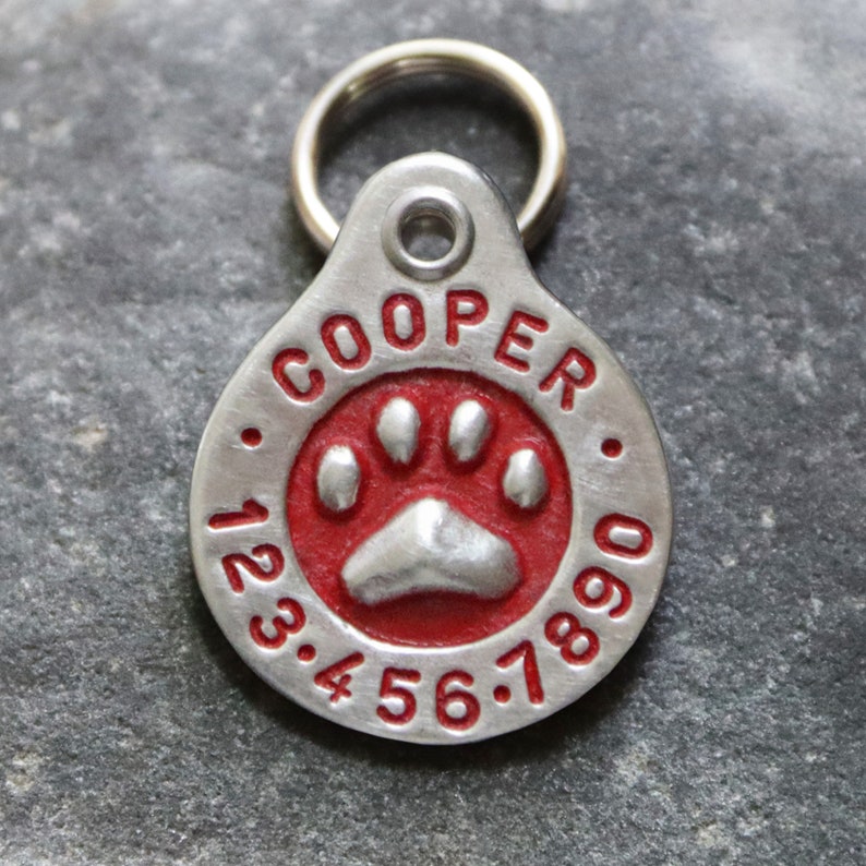 May include: Silver dog tag with a red paw print and the name "COOPER" and the numbers "123.456.7890" engraved on it.