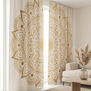 May include: A pair of floor-length curtains featuring a large, centered gold mandala print on a light beige fabric. The intricate circular pattern consists of repeating geometric shapes, petals, and fine lines that span across both curtain panels.
