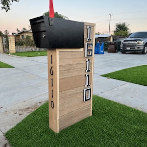 May include: A black metal mailbox with a red flag mounted on a rectangular wooden post structure. The post features horizontal wood planks and the house number 16110 displayed in large, bold, black and white vertical lettering on two sides.
