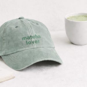 May include: A white ceramic mug with a black handle and the text "But First, Coffee" in a bold, black font. The mug is set against a blurred background, suggesting a cosy setting.
