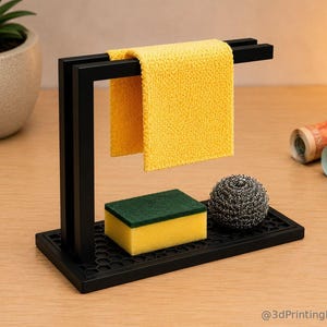 May include: A black rectangular sink caddy with a honeycomb-patterned base and an integrated vertical bar for hanging a yellow microfibre cloth. The caddy holds a rectangular yellow and green sponge and a round metallic scouring pad.