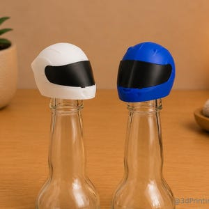 Könnte beinhalten: Zwei Flaschenverschlüsse in Form von Motorradhelmen, einer in Weiß und einer in Blau, jeweils mit einem schwarzen Visier. Die Verschlüsse sitzen auf zwei klaren Glasflaschen. Der Text 3dPrintingLabDE ist in der unteren rechten Ecke zu sehen.