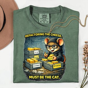 May include: Green Comfort Colors t-shirt featuring a cartoon mouse in glasses and a hoodie, holding cheese. The text says "Refactoring the Cheese. Must be the Cat." The shirt has a tag that says XL-TG-EG.