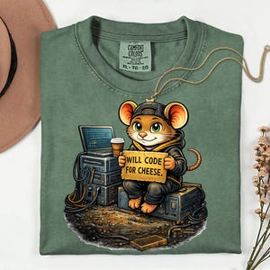 May include: Green Comfort Colors t-shirt with a cartoon mouse wearing a cap and hoodie, holding a sign saying "WILL CODE FOR CHEESE." The mouse is sat on computer equipment with a laptop and coffee cup.