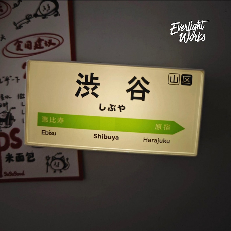 May include: A rectangular sign featuring the Japanese text Shibuya, the hiragana characters for Shibuya, and a green arrow pointing right. The sign displays the station names Ebisu, Shibuya, and Harajuku in both English and Japanese text.