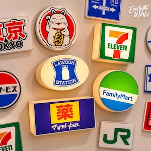 Könnte beinhalten: Eine Sammlung beleuchteter Wandschilder mit verschiedenen japanischen Markenlogos und Symbolen, darunter ein kreisförmiger Maneki-Neko, ein quadratisches 7-Eleven-Schild, ein ovales Lawson Station-Schild, ein kreisförmiges FamilyMart-Schild und ein rechteckiges Matsumoto Kiyoshi-Schild.