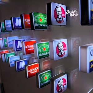 Peut inclure: Une exposition d'enseignes carrées éclairées présentant divers logos de marques. Les enseignes comprennent le logo Heineken avec un fond vert et une étoile rouge, le logo KFC avec le Colonel Sanders et d'autres enseignes avec du texte japonais. Les enseignes sont disposées en grille.