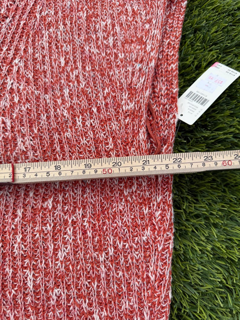 May include: Close-up of a red and white knit fabric. A measuring tape shows the fabric is approximately 24 inches wide. A price tag is attached to the fabric. The fabric has a textured appearance.