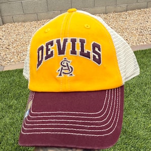 May include: A yellow and maroon baseball cap with the word "DEVILS" arched across the front in maroon lettering. The cap has a mesh back and a maroon bill with white stitching. The Arizona State University logo is below the word "DEVILS".