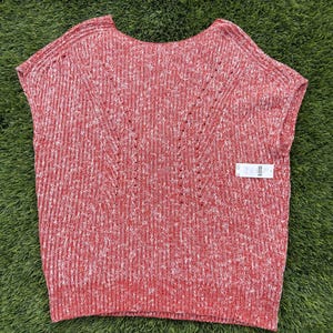 May include: Red and white knit sleeveless top. The top has a scoop neck and a textured knit pattern. The design includes a subtle V-shaped detail on the front. A tag is attached to the bottom right of the top.