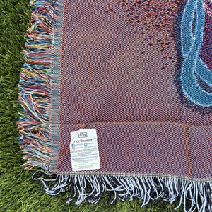 May include: Woven throw blanket with a colorful design and fringed edges. The blanket features a pattern in shades of red, blue, and brown. The edges are trimmed with a fringe of various colors. A tag with the brand name "northwest" is visible.