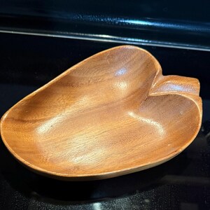May include: A wooden, leaf-shaped bowl with a smooth, polished surface. The bowl is made of a light brown wood and has a natural grain pattern. The bowl is approximately 8 inches long and 6 inches wide.