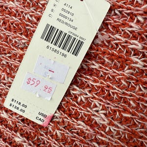 May include: Close-up of a red and white knit fabric. A tag is attached with the text "RED/ROUGE" and a barcode. The tag also shows the price of $59.95.