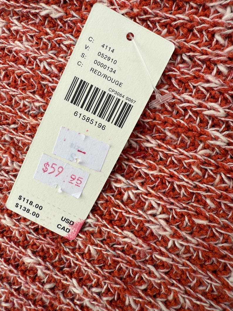 May include: Close-up of a red and white knit fabric. A tag is attached with the text "RED/ROUGE" and a barcode. The tag also shows the price of $59.95.
