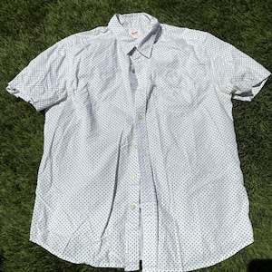 May include: White short-sleeved button-down shirt with a small, repeating navy blue polka dot pattern. The shirt has a classic collar and a red tag on the collar.