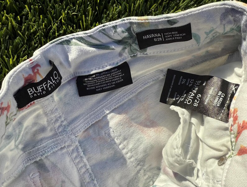 May include: Close-up of white denim ankle pants with a floral pattern. The pants have a high-rise fit and soft stretch. The brand label reads "BUFFALO DAVID BITTON". The size is 6/28.