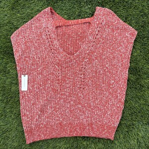 May include: A sleeveless red and white speckled knit sweater with a V-neck and a small cutout at the back of the neck. The sweater has a tag attached to the side. The sweater is made of a soft, comfortable material.