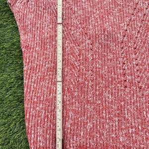 May include: Red and white knit sweater with a V-neck design. The sweater is approximately 27 inches long, measured with a wooden ruler. The fabric has a textured appearance with small holes throughout the design. The sweater is sleeveless.
