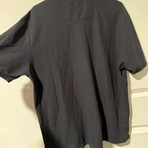 May include: A dark gray polo shirt with short sleeves. The shirt has a collar and a small pocket detail on the upper back. The fabric appears to be a soft, comfortable material.