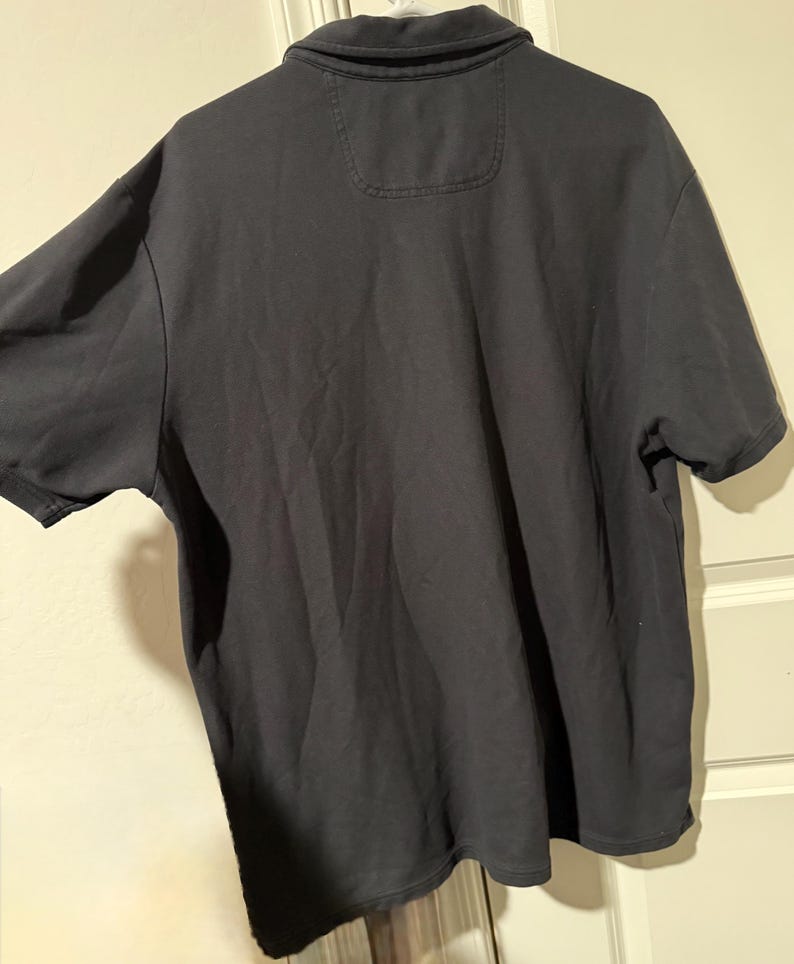 May include: A dark gray polo shirt with short sleeves. The shirt has a collar and a small pocket detail on the upper back. The fabric appears to be a soft, comfortable material.