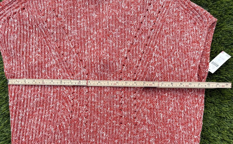 May include: Red and white knit sweater with a V-neck design. A wooden ruler is laid across the sweater, measuring approximately 24 inches. The sweater has a textured pattern and a tag attached.