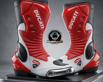 Könnte beinhalten: Paar rote, weiße und schwarze Ducati Motorradstiefel. Die Stiefel haben das Ducati-Logo und werden auf einer silbernen Plattform präsentiert. Die Stiefel sind aus Leder und haben ein schützendes Design.