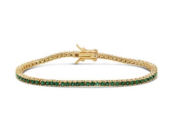 May include: A gold tennis bracelet featuring a continuous row of small, round, vibrant green gemstones set in a polished gold metal frame. The bracelet includes a secure, hinged box clasp mechanism at the top, designed to hold the chain together.
