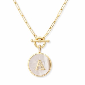 May include: Gold-tone necklace with a circular pendant featuring the letter "A" embellished with small crystals. The pendant has a mother-of-pearl background and is framed by a gold border. The necklace has a toggle clasp.