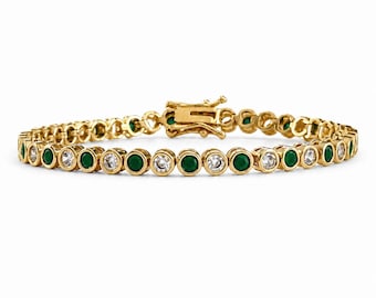 May include: A gold tennis bracelet featuring an alternating pattern of round, bezel-set green stones and clear, colorless stones. The bracelet is constructed with individual circular metal links and includes a secure box clasp mechanism at the center.