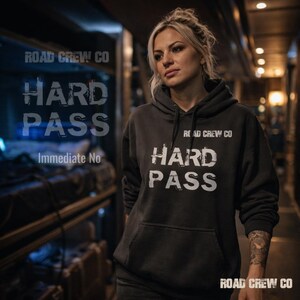 May include: A dark gray hoodie with the text "HARD PASS" in white, along with "ROAD CREW CO" printed above and below the text. The phrase "Immediate No" is also visible. The hoodie has a front pocket and a hood.