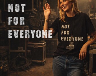 May include: A black t-shirt with the text "NOT FOR EVERYONE" in white. The shirt is part of the "ROAD CREW COLLECTION". The person is wearing blue jeans and smiling, waving their hand. The background includes equipment cases.