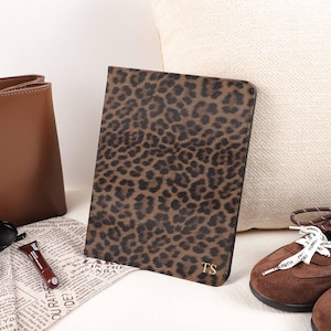 May include: A rectangular tablet or notebook cover featuring a brown and black leopard print pattern. The bottom right corner of the cover is embossed with the gold-colored initials TS. The cover has rounded corners and a slim, flat profile.