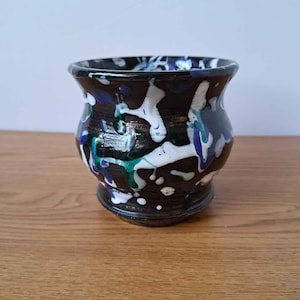 Peut inclure: Un petit pot en céramique arrondi avec une base brun foncé brillante. L'extérieur présente un motif décoratif éclaboussé dans des tons vifs de blanc, de bleu vif et de vert émeraude, créant un effet de gouttes multicolores contrasté.