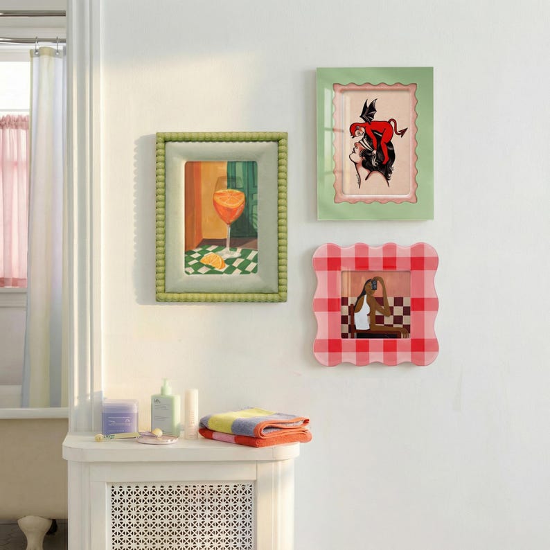 May include: Three wall-mounted picture frames. One rectangular frame with a beaded sage green border displays a cocktail illustration. A second rectangular frame with a scalloped light green border shows a red devil figure. A square frame with a red and white gingham scalloped border features a person taking a photo.