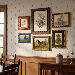 May include: A gallery wall arrangement featuring five rectangular picture frames with beaded edges in various colours including brown, blue, and green, surrounding botanical prints, a landscape sketch, and a painting of a brown horse.