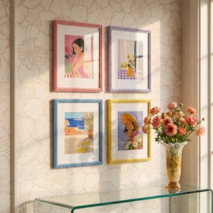 May include: Four rectangular wall frames with beaded edges in pink, purple, blue, and yellow, each containing a colorful illustration. The frames are arranged in a grid pattern on a wall, accompanied by a glass vase filled with pink flowers.